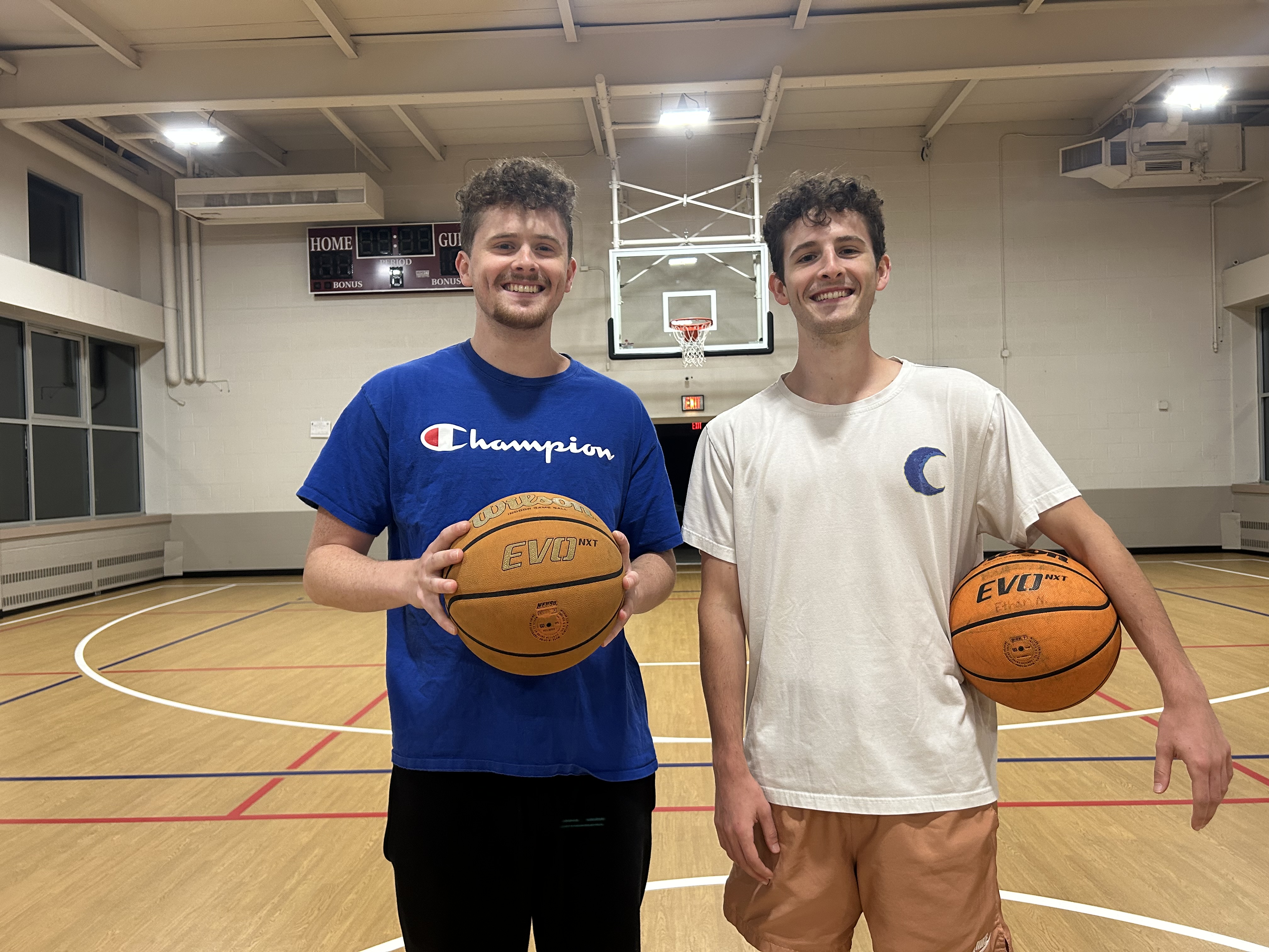 Coaches Sean and Connor Manning holding basketballs on the court at St. James Church Gym